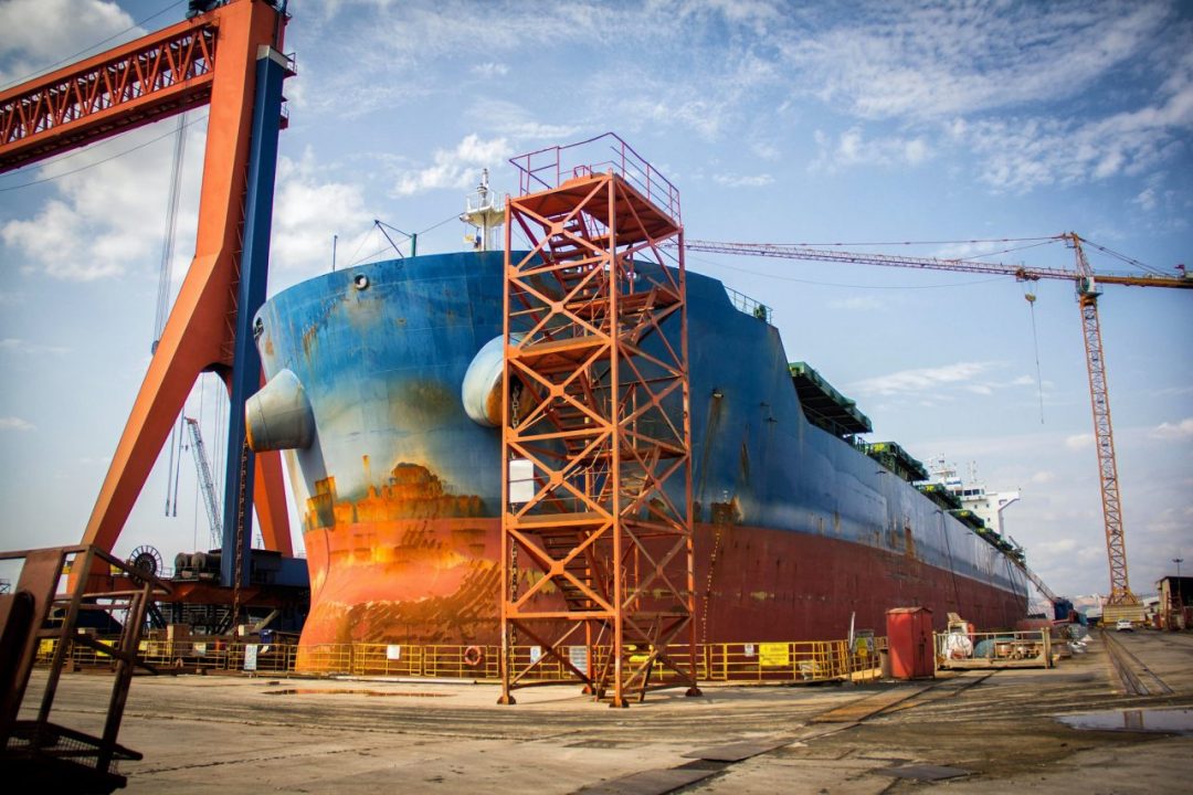 A large tanker cargo ship is being renovated and painted in shipyard dry dock